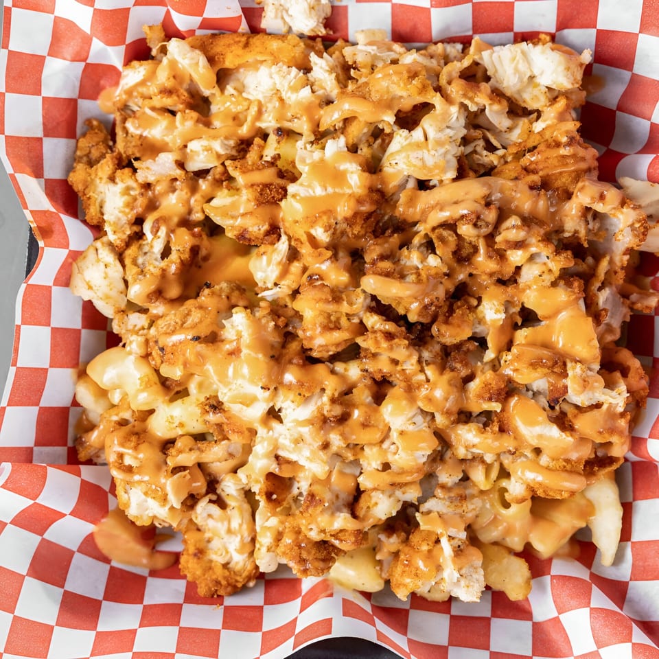 Papi's Hot Chicken's loaded fries with fried chicken pieces, macaroni, and cheese sauce in a red checkered basket.