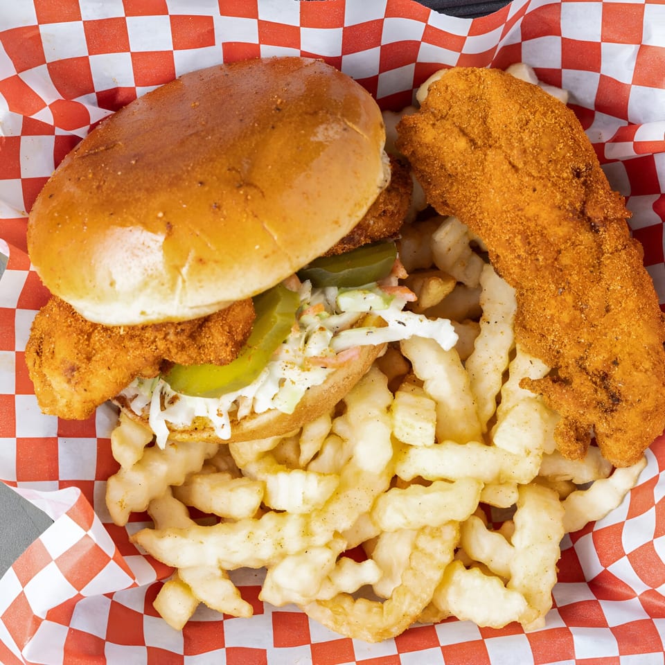 Papi's Hot Chicken sandwich with coleslaw and pickles, a fried chicken tender, and crinkle-cut fries.