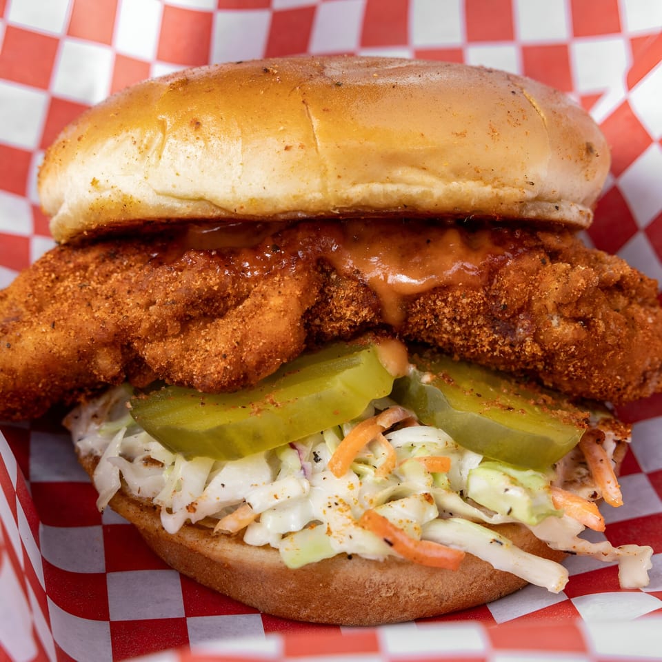 Papi's Hot Chicken sandwich with crispy fried chicken, pickles, coleslaw, and special sauce on a bun.
