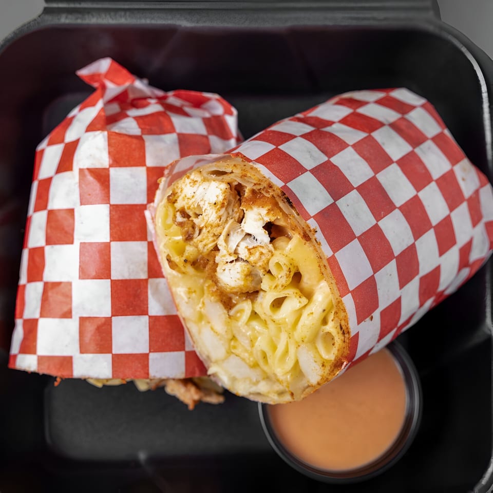 Papi's Hot Chicken burrito, filled with fried chicken and macaroni and cheese, in a black container.